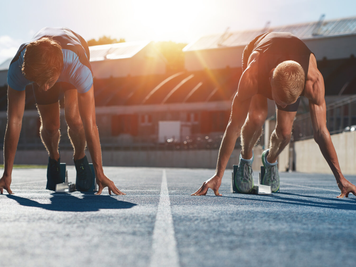 Sprinters at starting blocks ready for race . Athletes at starting position on athletics stadium race track with sun flare.
