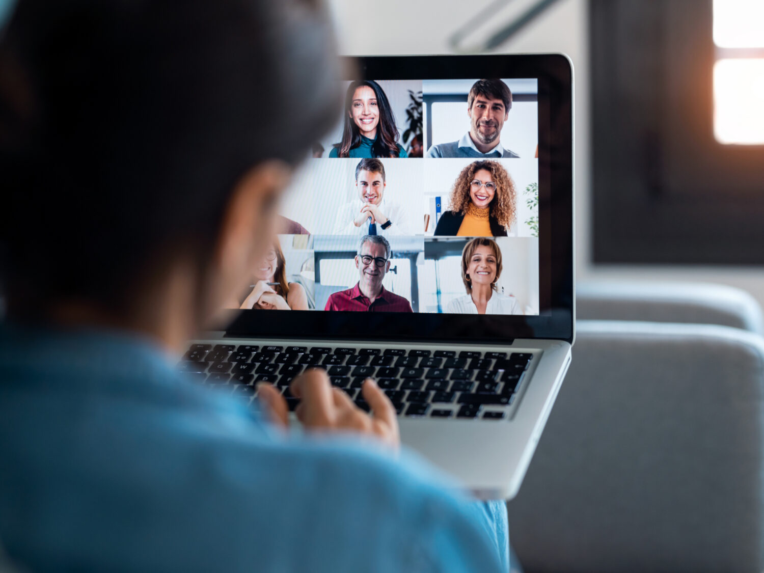 Back view of business woman speaking on video call with diverse colleagues on online briefing with laptop on sofa at home.