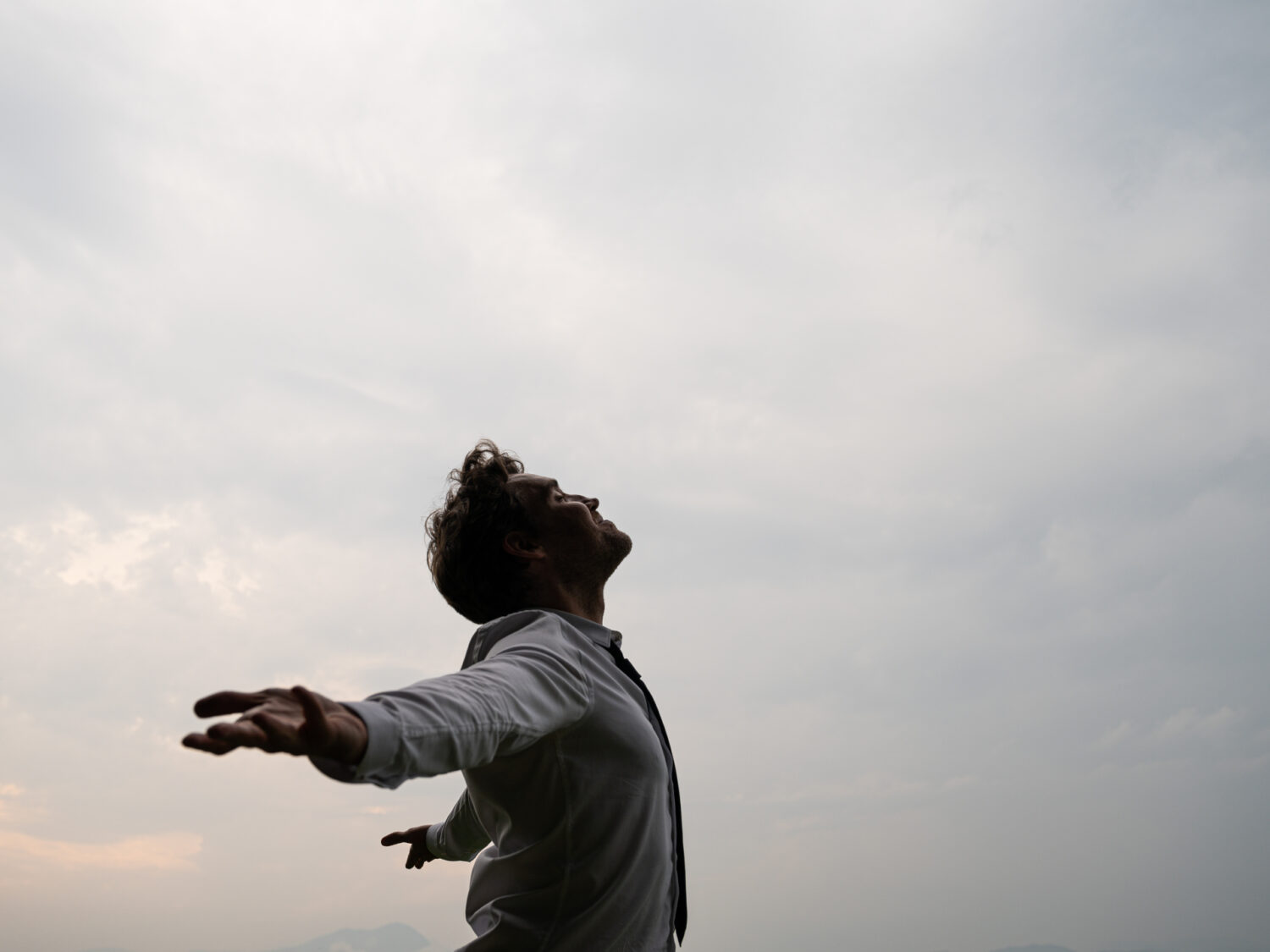 Peaceful young businessman standing with his arms spread looking up towards a cloudy sky.